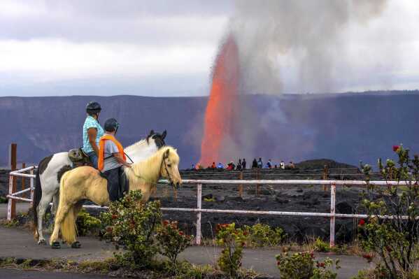 This photo provided by Janice Wei shows Candi Hololio Johnson, left, and Kim Kozuma, both on horseback, as they watch lava shooting out of Kilauea volcano's summit caldera inside Hawaii Volcanoes National Park, Hawaii, Wednesday, March 26, 2025. (Janice Wei via AP)