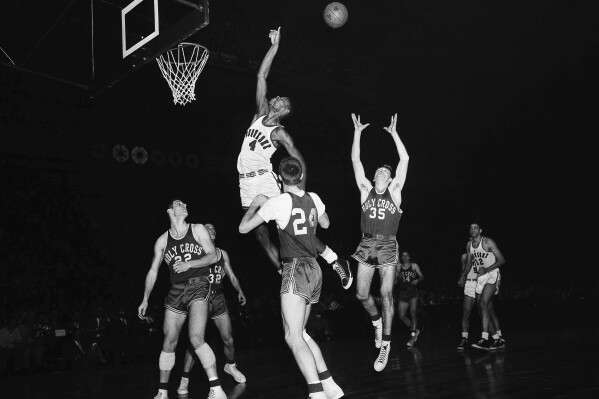 FILE - Duquesne center Jim Tucker (4) leaps for a rebound against Holy Cross players in the NIT finals at New York's Madison Square Garden, March 13, 1954. Holy Cross players, from left: Togo Palazzi (22); Joe Liebler (32); Tom Heinsohn (24) and Don Prohovich (35). Tucker was a part of a wave of Black players who helped the small Pittsburgh Catholic school become a national power in the 1940s and 1950s. (AP Photo/Marty Lederhandler, File)