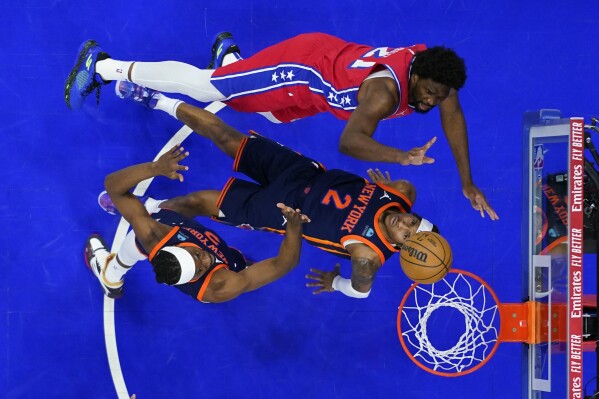 Philadelphia 76ers' Joel Embiid, top, goes up for a shot against New York Knicks' Miles McBride, center, and Precious Achiuwa during the first half of Game 4 in an NBA basketball first-round playoff series, Sunday, April 28, 2024, in Philadelphia. (AP Photo/Matt Slocum)