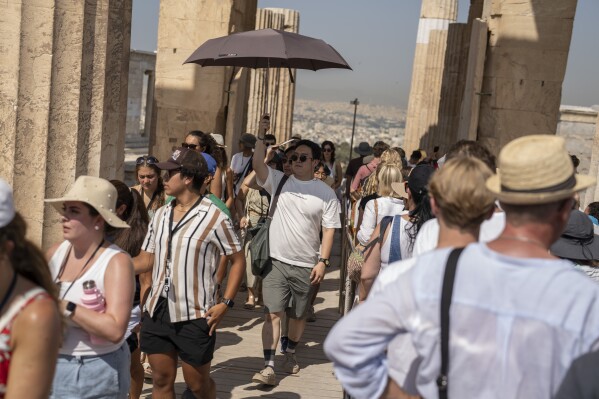 A man holds an umbrella as he and other tourists enters the ancient Acropolis hill during a heat wave, in Athens, Greece, Thursday, July 13, 2023. (AP Photo/Petros Giannakouris)