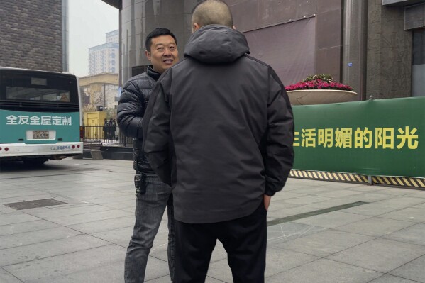 Plainclothes policemen have a chat as they stand watch outside the barricaded Sichuan Trust office building in Chengdu in southwestern China's Sichuan Province on Feb. 27, 2024. Some investors in a troubled trust fund in China are facing financial ruin under a government plan to return a fraction of their money, casualties of a slump in the property industry and a broader economic slowdown. (AP Photo/Andy Wong)