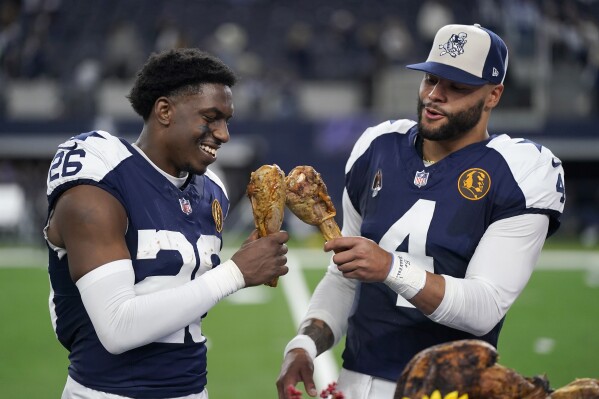 Dallas Cowboys cornerback DaRon Bland, left, and quarterback Dak Prescott celebrate by eating Thanksgiving turkey legs after the Cowboys defeated the Washington Commanders in an NFL football game Thursday, Nov. 23, 2023, in Arlington, Texas. (AP Photo/Sam Hodde)