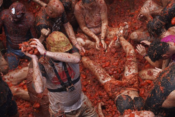 Revellers throw tomatoes at each other during the annual "Tomatina", tomato fight fiesta, in the village of Bunol near Valencia, Spain, Wednesday, Aug. 30, 2023. Thousands gather in this eastern Spanish town for the annual street tomato battle that leaves the streets and participants drenched in red pulp from 120,000 kilos of tomatoes. (AP Photo/Alberto Saiz)