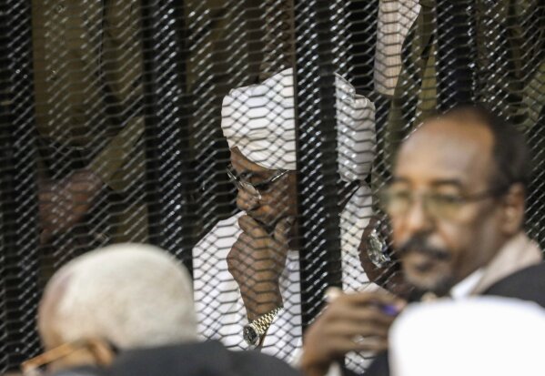 FILE - In this Aug. 24, 2019 file photo, Sudan's autocratic former President Omar al-Bashir sits in a cage during his trial on corruption and money laundering charges, in Khartoum, Sudan. A top Sudanese official said Monday, Feb. 11, 2020, that transitional authorities and rebel groups have agreed to hand over al-Bashir to the International Criminal Court for war crimes, including mass killings in Darfur. Since his ouster in April, al-Bashir has been in jail in Sudan’s capital, Khartoum over charges corruption and killing protesters. (AP Photo, File)