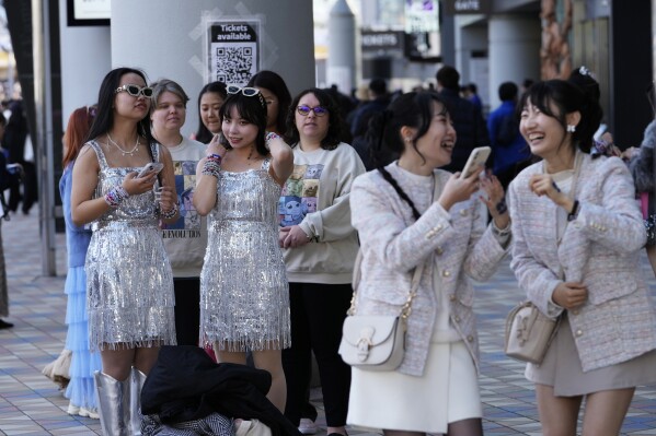 People wait in line near a poster to have their photos taken, while others, right, react to their selfies before Taylor Swift's concert at the Tokyo Dome in Tokyo, Saturday, February 10, 2024. (AP Photo/Hiro Kumai)