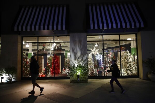 FILE - In this Dec. 16, 2019, file photo shoppers walk past a storefront with seasonal holiday products in Santa Clarita, Calif. Holiday shopping doesn't end with Christmas. Bargain hunters can take advantage of fatter discounts on clothing, home decor and other items between Christmas and well into January. (AP Photo/Marcio Jose Sanchez, File)