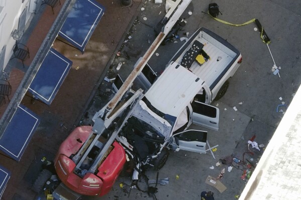 A black flag with white lettering lies on the ground rolled up behind a pickup truck that a man drove into a crowd on Bourbon Street in New Orleans, killing and injuring a number of people, early Wednesday morning, Jan. 1, 2025. (AP Photo/Gerald Herbert, File)