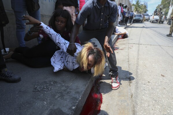 A woman cries after her friend, Valérie Saint-Fort, behind, fell dead from a bullet wound after soldiers fired their guns into the air as a tribute during the funeral of two soldiers in Port-au-Prince, Haiti, Monday, March 17, 2025. (AP Photo/Odelyn Joseph)