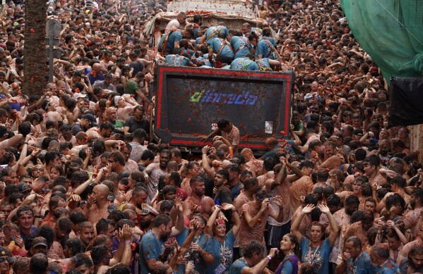 Revellers throw tomatoes at each other during the annual "Tomatina" tomato fight fiesta, in the village of Bunol near Valencia, Spain, Wednesday, Aug. 30, 2023. Thousands gather in this eastern Spanish town for the annual street tomato battle that leaves the streets and participants drenched in red pulp from 120,000 kilos of tomatoes. (AP Photo/Alberto Saiz)