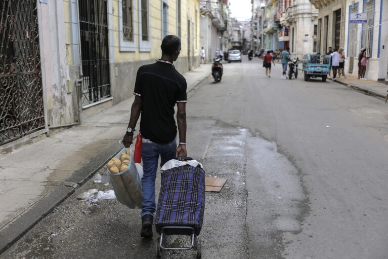 A man pulls a portable shopping cart while carrying a bag filled with bread, in Havana Cuba, Monday, March 11, 2024. Many Cubans feel ill-equipped to handle their new, more unequal country, a feeling that has worsened as small private markets have opened, charging prices similar to international ones in a country that hasn’t allowed non-state commerce in recent decades and where incomes remain between $16 and $23 monthly. (AP Photo/Ariel Ley)