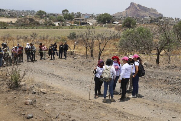 Women holding digging tools stand at the site where they said they found a clandestine crematorium, as the press and police stand by in Tlahuac, on the edge of Mexico City, Wednesday, May 1, 2024. A leader of one of the groups of so-called searching mothers from northern Mexico, announced late Tuesday that her team had found bones around clandestine burial pits and ID cards, and prosecutors said they were investigating to determine the nature of the remains. (AP Photo/Ginnette Riquelme)