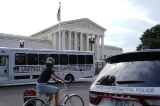 A bicyclist rides past police vehicles parked outside the U.S. Supreme Court building, Monday, June 27, 2022, in Washington. (AP Photo/Patrick Semansky)