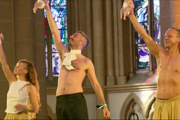 This grab taken from video shows performers dancing as they hold raw, plucked chickens wrapped in diapers, inside Paderborn's cathedral, Germany, Friday May 16, 2025. (RTL via AP)