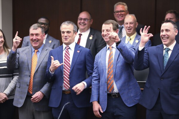 CORRECTS ID TO COASTAL CAROLINA WOMEN'S BASKETBALL COACH KEVIN PEDERSON, NOT COASTAL CAROLINA FOOTBALL COACH TIM BECK - From left to right, Clemson men's soccer coach Mike Noonan, South Carolina football coach Shane Beamer, Clemson football coach Dabo Swinney and Coastal Carolina women's basketball coach Kevin Pederson pose for photos with lawmakers before a meeting of a South Carolina House committee considering a bill allowing schools to help athletes with name, image and likeness deals on Tuesday, Feb. 6, 2024, in Columbia, S.C. (AP Photo/Jeffrey Collins)