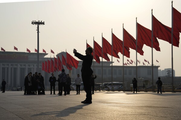 A man takes photos near red flags on Tiananmen Square before the closing session of the Chinese People's Political Consultative Conference (CPPCC) in Beijing, Sunday, March 10, 2024. (AP Photo/Ng Han Guan)