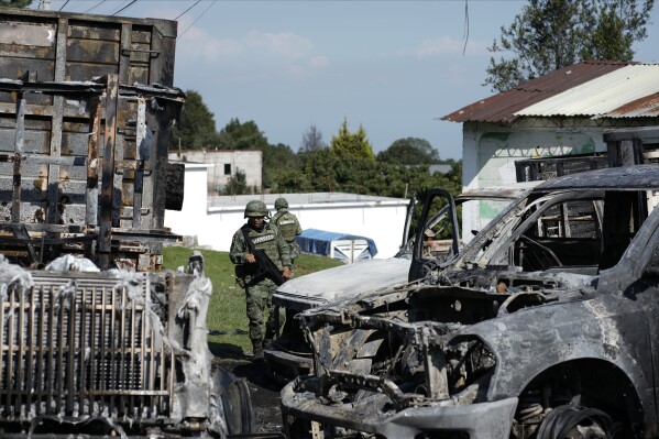 Mexican Army soldiers walk around the burnt-out remains of several trucks that were torched during a protest against a raid targeting illegal logging and sawmills in the pine forests outside of Huitzilac, Mexico, Wednesday, Aug. 2, 2023. Morelos state prosecutors said the raid involved at least 300 officers of the state police, the National Guard and the army. (AP Photo/Eduardo Verdugo)