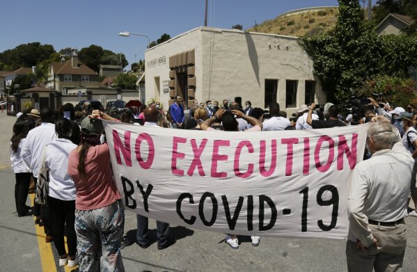 FILE - In this July 9, 2020, file photo, people hold up a banner while listening to a news conference outside San Quentin State Prison in San Quentin, Calif. One in five state and federal prisoners in the United States has tested positive for the coronavirus, a rate more than four times higher than the general population. In some states, more than half of prisoners have been infected, according to data collected by The Associated Press and The Marshall Project. (AP Photo/Eric Risberg, File)