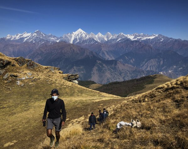 People wearing face masks trek up to Khalia top as snow clad Himalayan ranges of Panchchuli mountains are seen behind near Munsiyari in the Indian state of Uttarakhand, Thursday Oct. 29, 2020. India's confirmed coronavirus caseload surpassed 8 million on Thursday with daily infections dipping to the lowest level this week, as concerns grew over a major Hindu festival season and winter setting in. ( AP Photo/Manish Swarup)