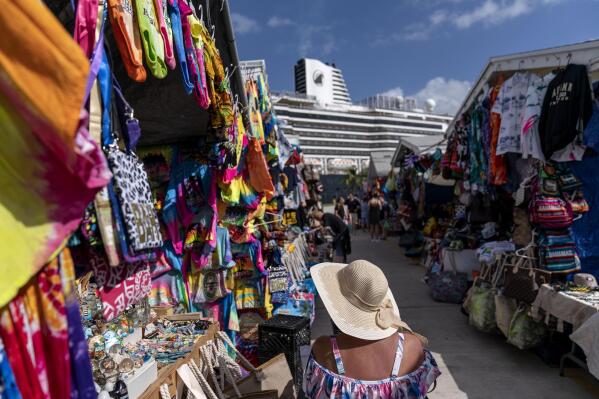 A tourist browses through a market at a cruise ship terminal in Freeport, Grand Bahama Island, Bahamas, Friday Dec. 2, 2022. Conch shells are a pillar of the island nation's economy and tourism industry. Dishes, spoons and art made from conch shells are for sale at street markets, and flags, T-shirts and hats depicting conch sell briskly to visitors. (AP Photo/David Goldman)
