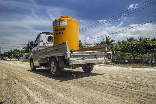 A truck carrying a water tank sprays the dirt road to reduce dust at Mangkupadi village near the construction site of the Kalimantan Industrial Park Indonesia (KIPI) in North Kalimantan, Indonesia on Thursday, Aug. 24, 2023. (AP Photo/Yusuf Wahil)