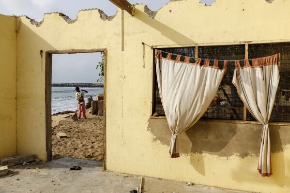 A girl sweeps the compound of an 80-year-old family home impacted by coastal erosion in Avegadzi, Ghana, Wednesday, March 5, 2025 (AP Photo/Misper Apawu)