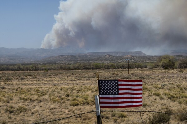 FILE - An American Flag on a fence blows in the wind along NM 22 as the Cerro Pelado Fire burns in the Jemez Mountains, April 29, 2022, in Cochiti, N.M. The U.S. Forest Service said on Monday, July 24, 2023, that its own prescribed burn started the 2022 wildfire that nearly burned into Los Alamos, N.M. (Robert Browman/The Albuquerque Journal via AP, File)
