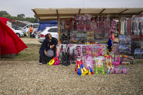 An elderly woman waits for customers at a fair in Hagioaica, Romania, Saturday, Sept. 16, 2023. For many families in poorer areas of the country, Romania's autumn fairs, like the Titu Fair, are one of the very few still affordable entertainment events of the year. (AP Photo/Vadim Ghirda)