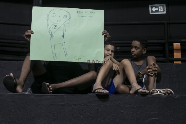 Children hold drawings that represent their experiences of living in the Mare favela at an event to launch the book titled “I was supposed to be at school” in the Mare favela of Rio de Janeiro, Brazil, Monday, March 25, 2024. Dozens of kids and teenagers from one of Rio de Janeiro's most violent favelas gathered on Monday to celebrate their most important piece of work yet: a book that aims to show authorities how they see police violence in their Maré community from a young age. (AP Photo/Bruna Prado)