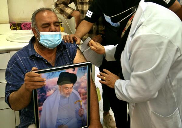 A follower of populist Shiite cleric Muqtada al-Sadr holds a picture of him while receiving a dose of the Chinese Sinopharm coronavirus vaccine at a clinic in Sadr City, Baghdad, Iraq, Wednesday, May 4, 2021. Iraq’s vaccine rollout had been faltering for weeks. Apathy, fear and rumors kept many from getting vaccinated despite a serious surge in coronavirus infections and calls by the government for people to register for shots. It took al-Sadr’s public endorsement of vaccinations — and images of him getting the shot — to turn things around. (AP Photo/Hadi Mizban)