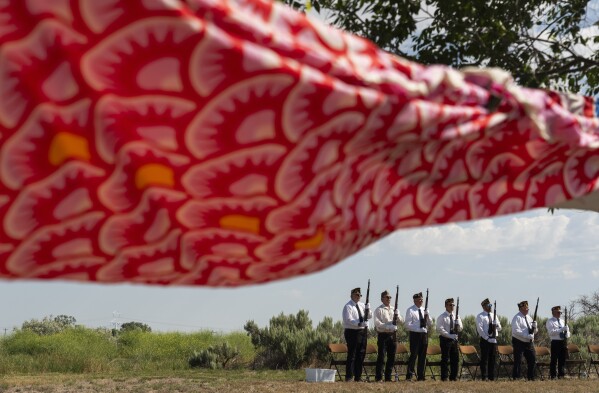 An honor guard from the American Legion Post #41 from Wendell, Idaho, prepares for a rifle salute as a large koinobori, or carp flag, flies in the wind during a closing ceremony for the Minidoka Pilgrimage at the Minidoka National Historic Site, Sunday, July 9, 2023, in Jerome, Idaho. (AP Photo/Lindsey Wasson)