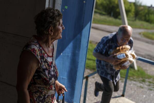 Vasyl Moiseienko, a retiree, right, carries fresh loaves of bread as an elderly resident waits for his delivery at a shop in Dyliivka, Donetsk region, eastern Ukraine, Saturday, Aug. 20, 2022. (AP Photo/David Goldman)