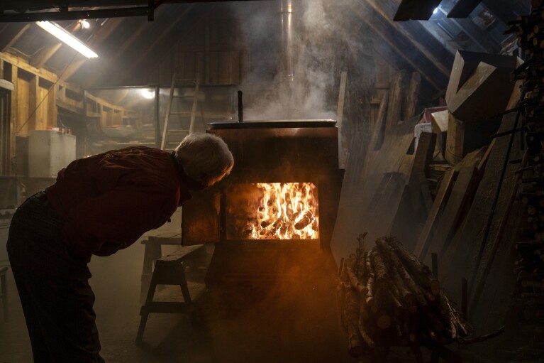 Brent Hosking checks the fire burning in his sugarhouse while boiling a batch of sap to make maple syrup Sunday, March 3, 2024, in Elmore, Vt. Hosking helped start the fire department in 1983 after locals tired of paying neighboring towns to extinguish fires. Being involved has helped foster a sense of community, Hosking says. Town Meeting helps foster that sense of community, he says. It's a time to get to know your neighbor, he says, which is important in a small town.(AP Photo/David Goldman)