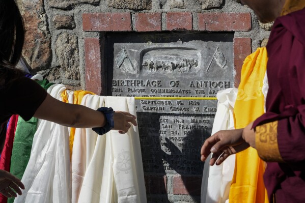 Buddhist faith leaders and community members drape Tibetan prayer scarves on the Birthplace of Antioch marker during the "May We Gather" pilgrimage, Saturday, March 16, 2024, in Antioch, Calif. The event aimed to use karmic cleansing through chants, prayer and testimony to heal racial trauma caused by anti-Chinese discrimination in Antioch in the 1870s. (AP Photo/Godofredo A. Vasquez)