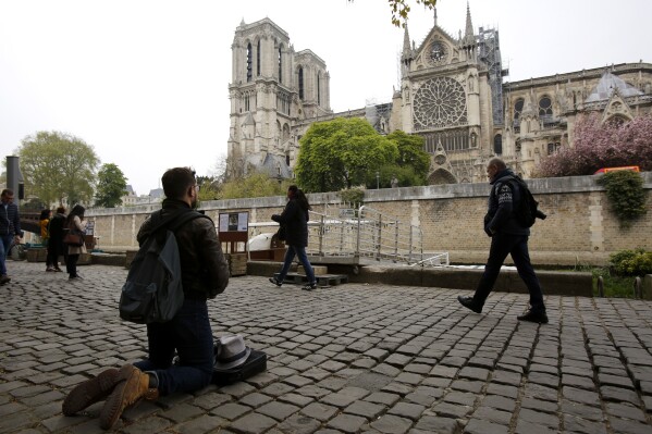 FILE - A man kneels to pray by the Notre Dame cathedral after the fire in Paris, Tuesday, April 16, 2019.The restoration of Notre Dame hits a milestone Friday, Dec. 8, 2023: one year until the cathedral reopens its huge doors to the public. (AP Photo/Christophe Ena, File)