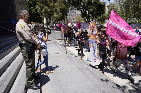 A Los Angeles County Sheriff's deputy watches a procession of Britney Spears supporters march outside a court hearing concerning the pop singer's conservatorship at the Stanley Mosk Courthouse, Wednesday, June 23, 2021, in Los Angeles. (AP Photo/Chris Pizzello)