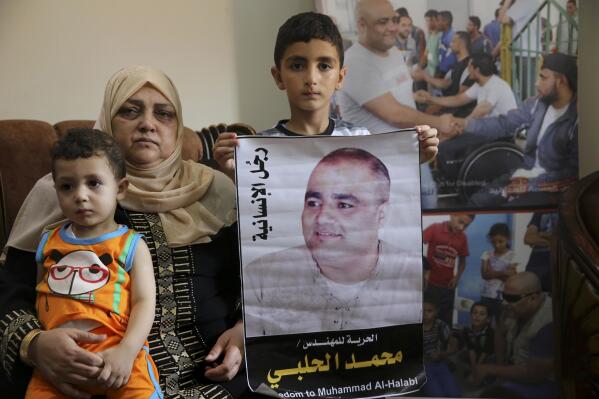 FILE - Amal el-Halabi holds her grandson Fares while her grandson Amro, 7, holds a picture of his father Mohammed el-Halabi, Gaza director of the international charity World Vision, who is detained and accused by Israeli security of diverting sums to Hamas that exceed its total budget, at his family house in Gaza City, Aug. 8, 2016. In May 2022, nearly six years after Israel accused Mohammed el-Halabi of diverting tens of millions of dollars from an international charity to Gaza's militant Hamas rulers, he has yet to be convicted in an Israeli court and is still being held in detention. World Vision as well as independent auditors and the Australian government, have found no evidence of any wrongdoing. Arabic on the picture reads, " the man of humanity."  (AP Photo/Adel Hana, File)