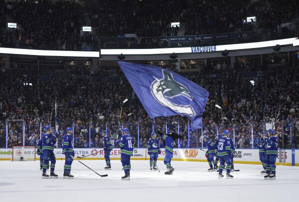 Vancouver Canucks players gather at center ice to raise their sticks to the fans after defeating the Calgary Flames in the team's home regular-season finale NHL hockey game Tuesday, April 16, 2024, in Vancouver, British Columbia. (Darryl Dyck/The Canadian Press via AP)