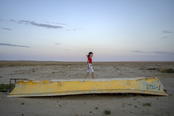 A girl plays on a worn-out boat along the dried-up Aral Sea, in the village of Tastubek near Aralsk, Kazakhstan, Monday, July 2, 2023. (AP Photo/Ebrahim Noroozi)