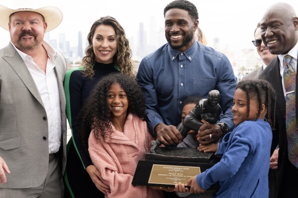 Former USC football player Reggie Bush poses with his attorneys, left, Levi McCathern and Ben Crump, right, along with his and family and his Heisman trophy during a news conference at the Los Angeles Memorial Coliseum, Thursday, April, 25, 2024, in Los Angeles. (AP Photo/Richard Vogel)