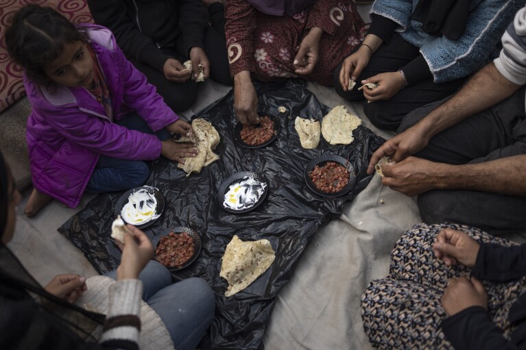 Members of the Abu Jarad family, who were displaced by the Israeli bombardment of the Gaza Strip, eat breakfast at a makeshift tent camp in the Muwasi area, southern Gaza, Monday, Jan. 1, 2024. (AP Photo/Fatima Shbair)