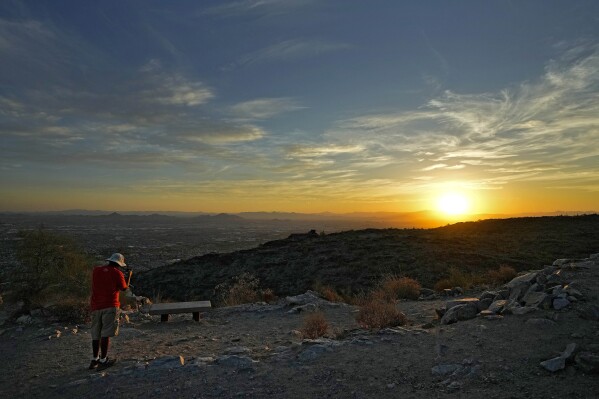 A hiker photographs the sun rising over the Valley atop South Mountain, Monday, July 17, 2023 Phoenix. Phoenix is set to break its own record for consecutive days of highs of at least 110 degrees. Around one-third of Americans are under some type of heat advisory, with the most blistering temperatures in the South and West, where even the regular simmer has turned up a notch. (AP Photo/Matt York)