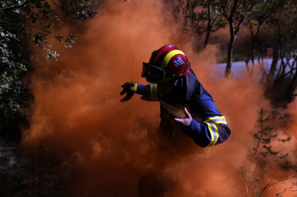 A firefighter leaves the area after lighting a smoke flare during a preparedness drill at Glyka Nera, in northeastern Athens on Thursday, April 4, 2024. Authorities have stepped up exercises ahead of the official start of the fire season on May 1. (AP Photo/Thanassis Stavrakis)