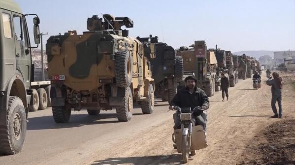 In this frame grab from video taken on Sunday, Feb. 2, 2020, people ride their motorcycles next to a Turkey Armed Forces convoy is seen at the northern town of Sarmada, in Idlib province, Syria. A large Turkish military convoy moved into the rebel-held areas of northwest Syria on Sunday, witnesses on the ground said, adding it appeared to be heading towards the south of Idlib province. (AP Photo/APTN)
