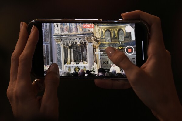 A woman takes photos with her phone to Pope Leo XIV presides over a Mass in the Archbasilica of St. John Lateran and takes possession of the Roman Cathedra, formalising his role as Bishop of Rome in Rome, Sunday, May 25, 2025. (AP Photo/Gregorio Borgia)