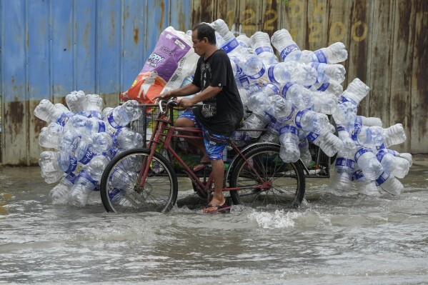 FILE - A man uses his pedicab to transport used plastic containers along a flooded street in Valenzuela city, Philippines, Aug. 2, 2023. (AP Photo/Aaron Favila, File)