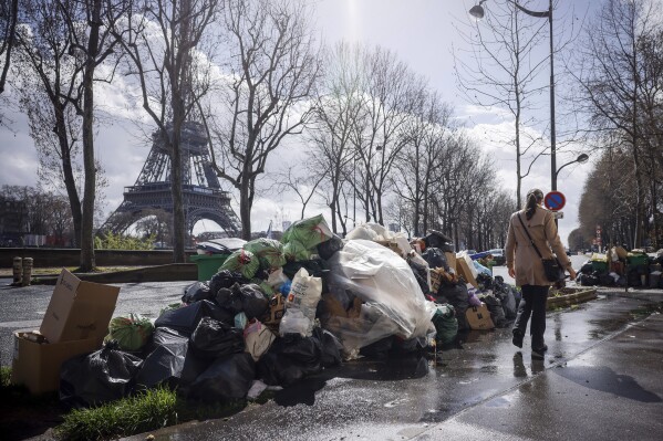 FILE - A woman walks past a pile of uncollected garbage near Eiffel Tower in Paris, Friday, March 24, 2023. Paris garbage collectors have lifted the strike notice that threatened to leave the French capital city under piles of junk during the Olympic Games after striking a deal that will improve their pay. Paris City Hall said in a statement on Wednesday, May 15, 2024 it sealed a deal with the workers and that the strike notice covering several days in May and a period from July to Sept. 8 had been lifted (AP Photo/Thomas Padilla, File)