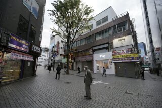 FILE - In this April 24, 2020, file photo, a man wearing a face mask to help stop the spread of the new coronavirus stands in a middle of a walking street in the Shinjuku ward in Tokyo. Recession-hit Japan's exports plunged nearly 22% in April, the country's worst drop in more than a decade as the coronavirus pandemic slammed global demand, the Finance Ministry said Thursday, May 21, 2020. (AP Photo/Eugene Hoshiko, File)