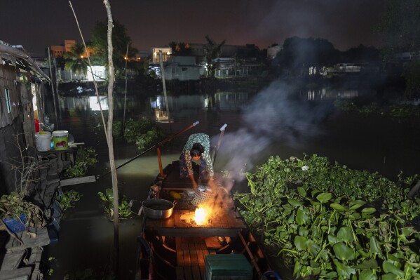 Nguyen Thi Thuy, a vendor selling steamed buns on a floating market, ignites a fire on her boat while getting ready for her day's work in Can Tho, Vietnam, Wednesday, Jan. 17, 2024. (AP Photo/Jae C. Hong)