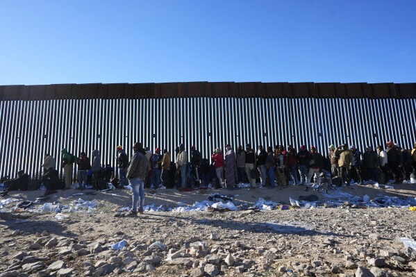 Hundreds of migrants gather along the border wall Tuesday, Dec. 5, 2023, in Lukeville, Ariz. The U.S. Border Patrol says it is overwhelmed by a shift in human smuggling routes, with hundreds of migrants from faraway countries like Senegal, Bangladesh and China being dropped in the remote desert area in Arizona. (AP Photo/Ross D. Franklin)
