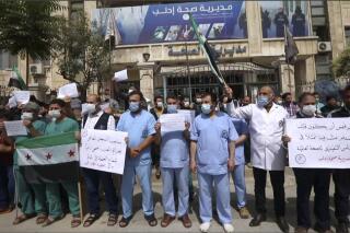 In this image taken from video, dozens of medical workers protest a decision to grant Syrian President Bashar Assad’s government a seat on the executive board of the World Health Organization, Monday, May 31, 2021, in Idlib, Syria.  (AP Photo)